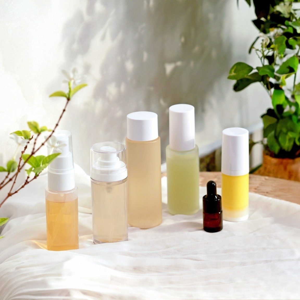 A collection of skincare products displayed on a soft fabric, with greenery in the background.